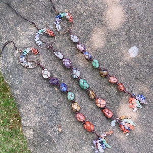 Three handmade Tree of Life chakra crystal wall hangings with natural stones on a stone background