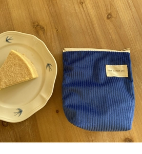 Detail van blauwe corduroy make-up tas met metalen rits op houten bureau
