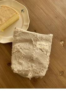 Detail van beige canvas mini-tasje met franje-textuur en label op een houten tafel