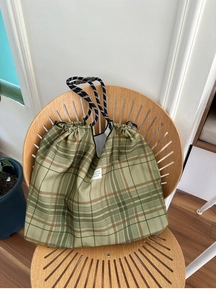 Detail of green checkered drawstring tote bag with thick rope handles and woven label