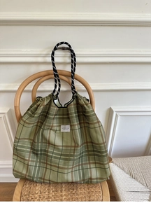 Detail of dark green plaid canvas tote bag featuring unique thick rope handles on wooden chair