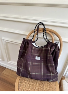 Detail of checkered tote bag with drawstring closure hanging on a wicker chair