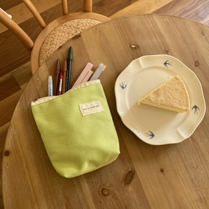 Groene canvas etui met 'nice to meet you' label en pennen op een houten tafelblad