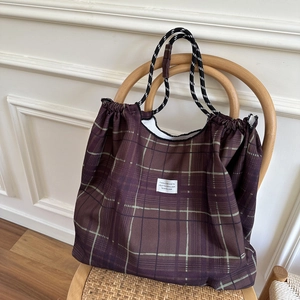 Brown plaid tote bag with drawstring closure and braided ropes on vintage wooden chair
