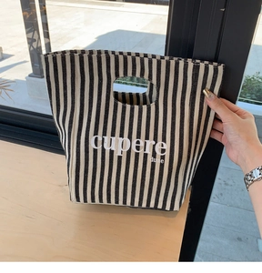 Dettaglio della borsa tote in tela a righe con manico ovale e logo su tavolo in legno