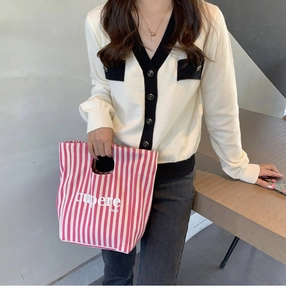 Dettaglio della borsa in tela a righe rosa e bianche con scritta e cardigan in maglia