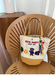 Detail of canvas tote bag with animal embroidery and smile doll charm on a wooden chair
