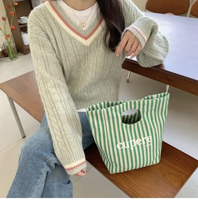 Dettaglio della trama del maglione verde chiaro e della borsa tote in tela a righe verdi
