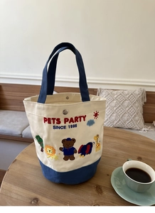 Detail of canvas lunch bag featuring colorful animal embroidery and navy blue handles