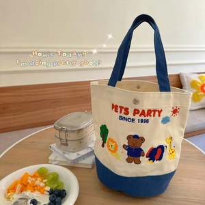 Canvas lunch tote bag with animal embroidery and navy blue handles on a wooden table