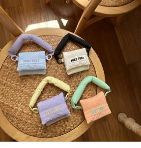 Quilted mini earphone bags in four colors with JUST THAT embroidery on a woven stool