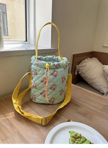 Detail of mint green quilted bucket bag with brown bear prints and yellow straps