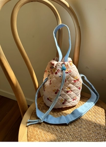 Detail of pink quilted bucket bag with cherry and bear pattern on a wooden chair