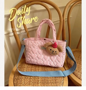 Detailed close-up of pink heart-quilted handbag with blue strap and cute bear charm