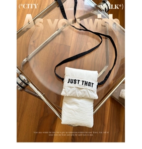 Close-up of a white canvas phone bag featuring JUST THAT lettering on a stylish chair