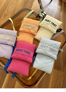 Detailed view of colorful nylon crossbody phone bags in five vibrant shades on amber tray