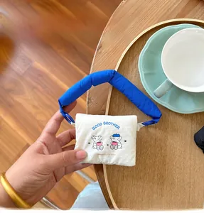 Mini fabric pouch with cartoon dog print and blue handle held in hand for scale