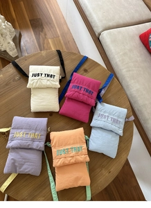 Detail of colorful canvas crossbody bags with embroidered Just That text on fabric