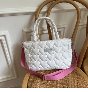 Detail view of white heart-quilted puffer tote bag with pink strap on a wooden chair