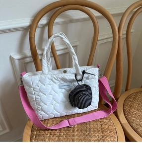 Detail of white heart-quilted puffer bag with adjustable pink strap on vintage chair