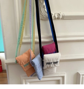 Detailed view of colorful mini fabric crossbody bags with embroidered text on a white wall