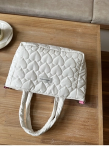Close-up of white quilted handbag with heart embroidery and stylish woven label detail