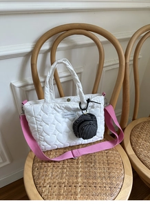 Detail of white quilted heart pattern bag with pink strap and mini hat charm on a chair