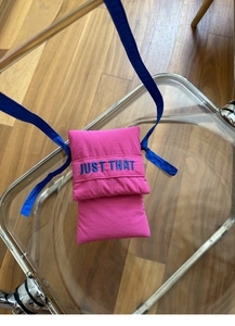 Detail showing raspberry pink mini phone bag with blue embroidered JUST THAT text and strap