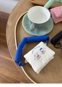 Close-up of quilted white mini pouch with blue handles and cartoon bears on wooden table