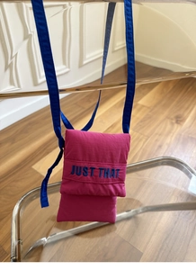 Close-up of pink fabric phone bag featuring blue 'JUST THAT' embroidery and strap