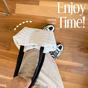 Detailed top view of white quilted tote bag with heart pattern and black straps on wood floor