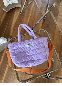 Detail of purple heart quilted tote bag with orange strap on a transparent chair