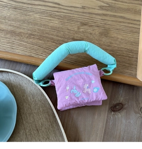 Detailed view of purple cartoon mini bag with mint green handle on wooden desk