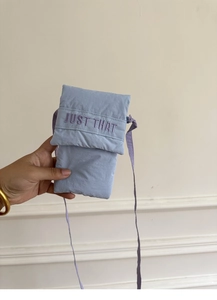 Close-up of light purple nylon phone bag with JUST THAT embroidery and flap closure
