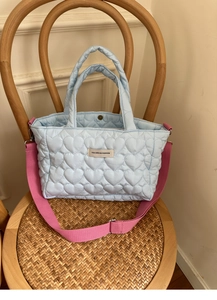 Detail of heart-quilted light blue tote bag with a contrasting pink crossbody strap