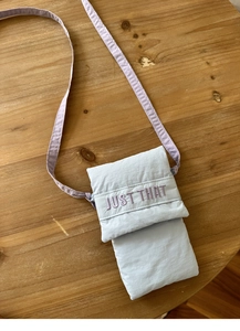 Detail of light blue quilted phone bag with purple 'JUST THAT' embroidery on fabric