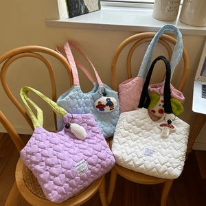 Detailed view of heart-quilted canvas tote bags in macaron colors on wooden chairs