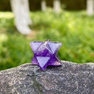 Natural 20mm amethyst merkaba star crystal gemstone placed on a natural rock outdoors