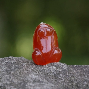 Natural red agate crystal sun bear pendant with silver clasp on a natural stone background