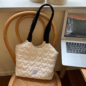 Detail of white heart-quilted canvas tote bag with black handles on a wooden chair