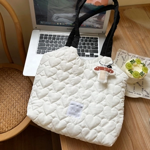 Detail of heart-quilted white tote bag with wide black strap and mushroom charm accessory