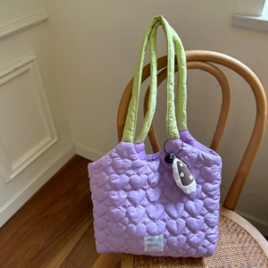 Close-up of lilac quilted tote bag with heart patterns and light green handle on wooden chair