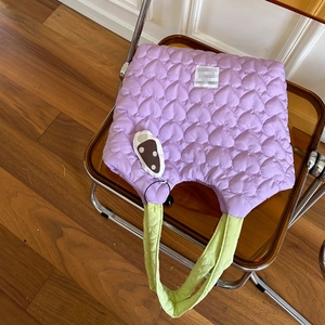Detail of purple heart-quilted canvas tote with green contrast handles on a chair