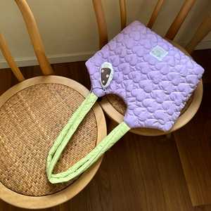 Detail of purple heart quilted handbag with contrasting green padded straps on a chair