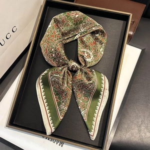 Détail d'un foulard en soie à motif paisley vert forêt et marron sur un plateau chic