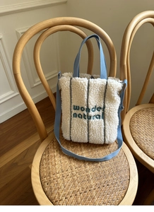 Close-up of cream faux shearling tote with green wonder embroidery and light blue strap