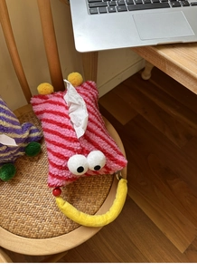 Detail of red and pink striped plush monster tissue box with cartoon eyes on a chair