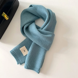 Dettaglio di sciarpa in maglia blu Morandi con etichetta in tessuto emo minimalista
