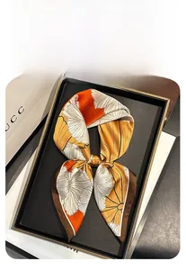 Detail of a 70cm square silk scarf with floral prints in orange and gold on a tray
