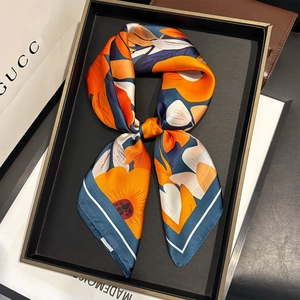 Close-up of silk satin square scarf with orange and blue floral pattern on black tray